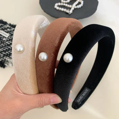 three padded headbands in beige, brown, and black, each with a pearl accent, held in a hand