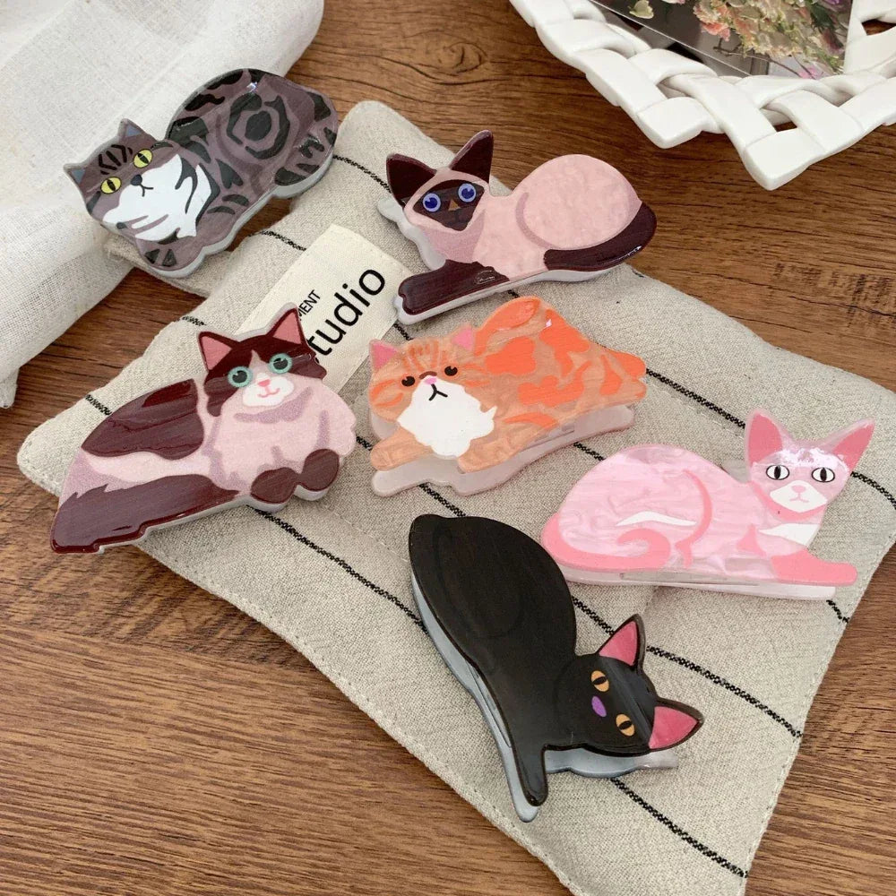 A group of cat-shaped hair clips are arranged on a textured fabric.