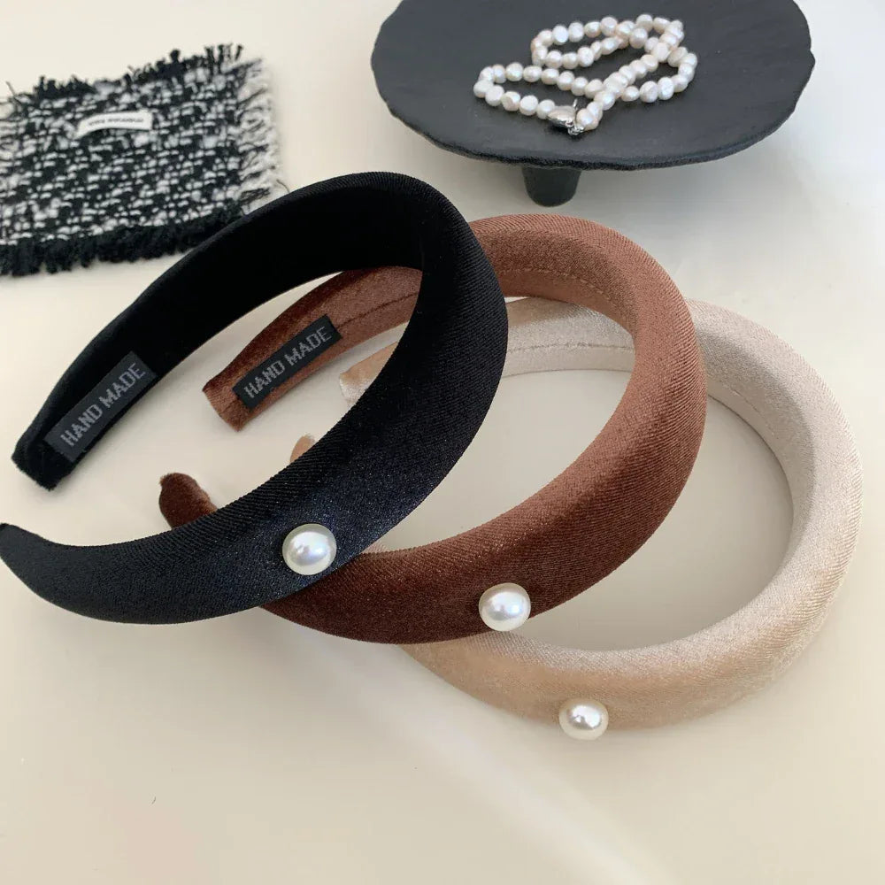 three padded headbands in black, beige, and brown, with pearl accents, next to a pearl necklace