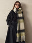 woman wearing a long dark coat and a green and white plaid scarf draped around her neck