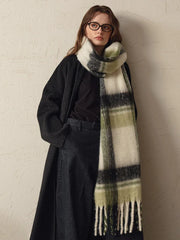 woman wearing a long dark coat and a green and white plaid scarf draped around her neck
