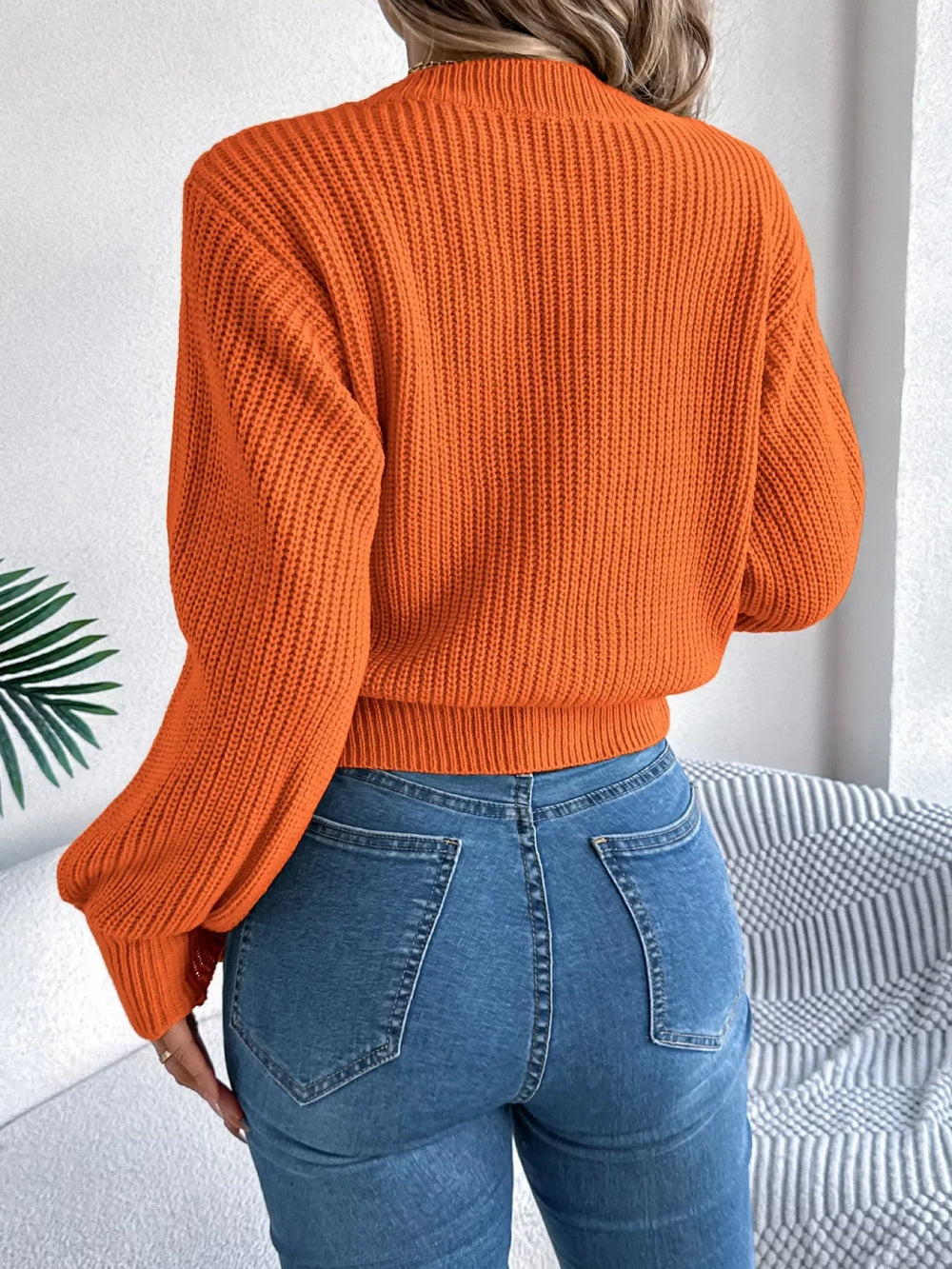 Back view of a woman wearing an orange cable knit sweater with blue jeans