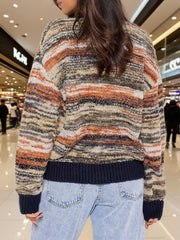 Back view of a woman wearing a multicolored striped knit cardigan with a V-neck and button-up front, paired with light-wash jeans.