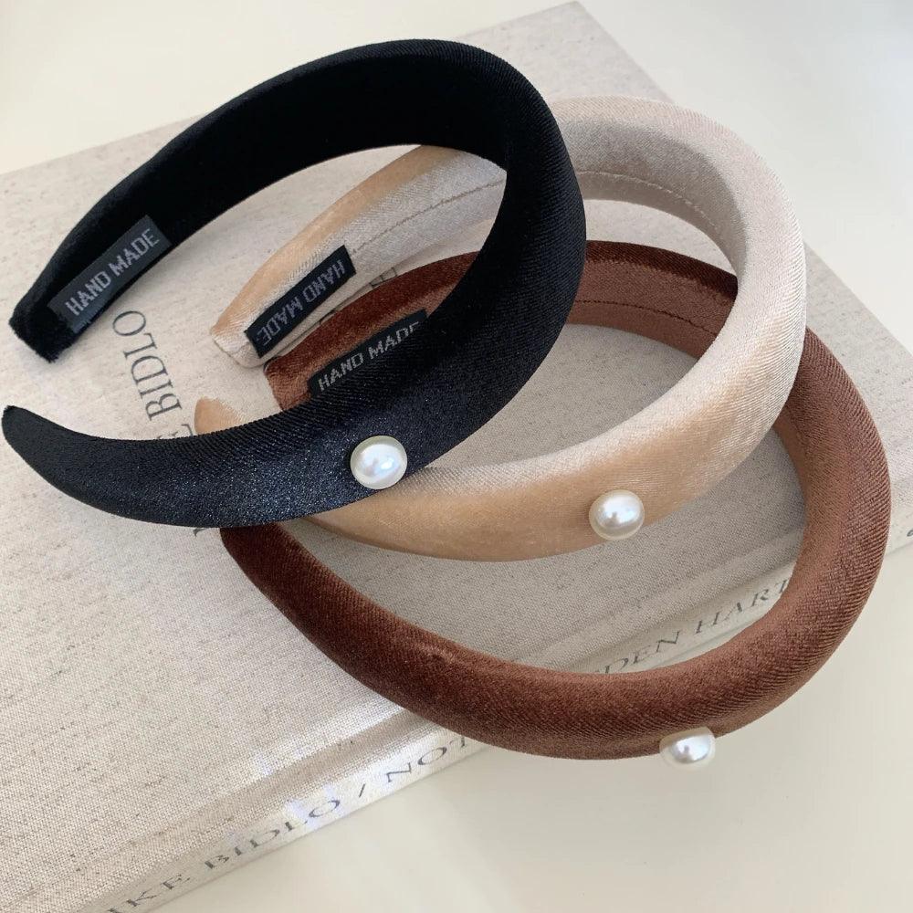 three padded headbands in black, beige, and brown, with pearl accents, placed on a book