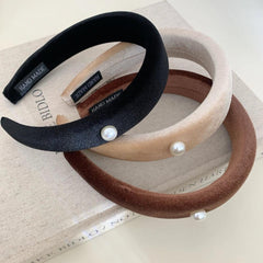 three padded headbands in black, beige, and brown, with pearl accents, placed on a book