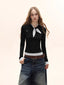 Model wearing a black long-sleeve top with a white polka dot scarf detail and white polka dot cuffs, paired with denim jeans and a brown belt.