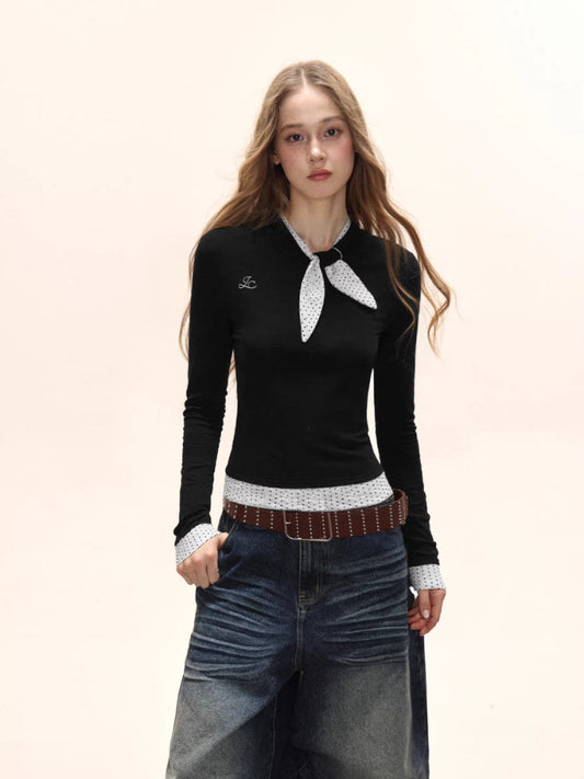 Model wearing a black long-sleeve top with a white polka dot scarf detail and white polka dot cuffs, paired with denim jeans and a brown belt.