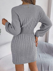 Back view of a woman wearing a grey cable knit sweater dress with a cinched waist.