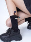 Black crew socks with a black creature applique and pom-pom accents, paired with black sneakers.