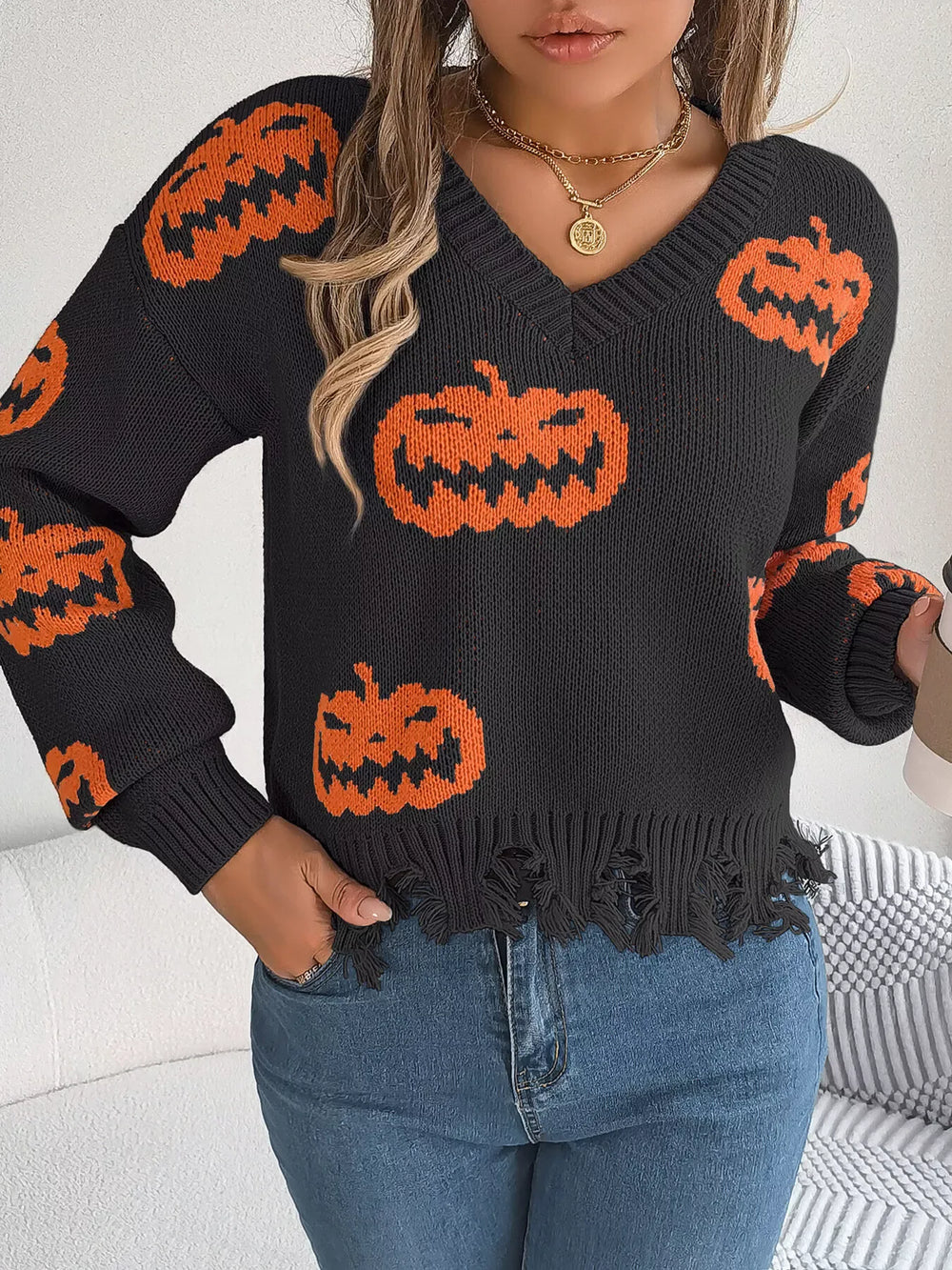 Woman wearing a black long-sleeve v-neck cropped knit sweater with an all-over orange pumpkin print and a distressed hem, holding a coffee cup.