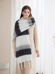 Woman modeling a cream coat and a versatile, oversized striped scarf in white, grey, and dark blue.