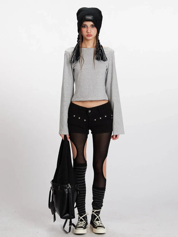 Model wearing a grey and white striped long-sleeved cropped top with flared sleeves, black shorts with cut-outs, black and grey striped thigh-high socks, and black sneakers. She is also wearing a black beanie and carrying a black bag.