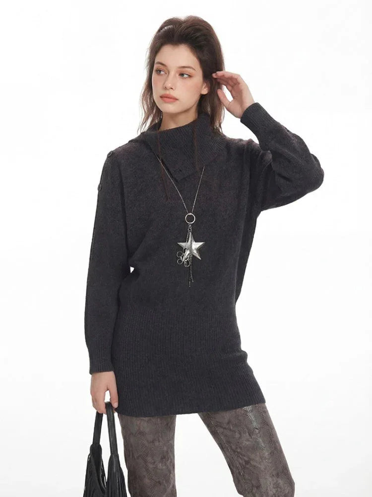 Model posing in a charcoal grey oversized turtleneck knit tunic, showcasing the texture and neckline, with a hint of the patterned leggings and leg warmers below.