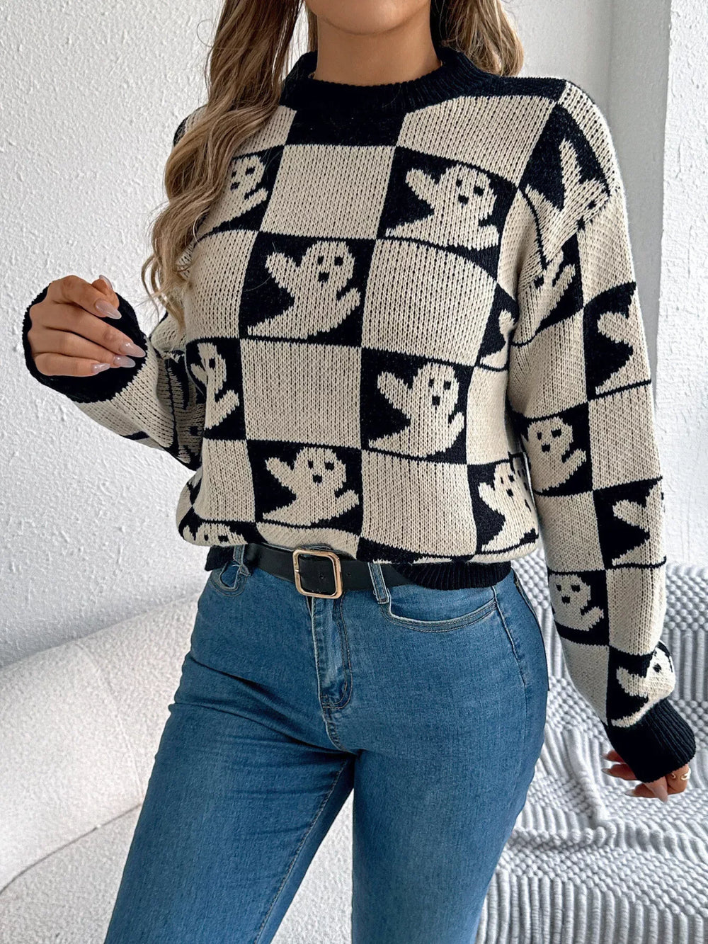 Woman adjusting her hair while wearing a black and white ghost print checkerboard knit sweater with blue jeans.