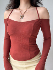 Woman in a rust-colored ribbed knit top with off-the-shoulder long sleeves and a halter neckline, showcasing the fitted silhouette.