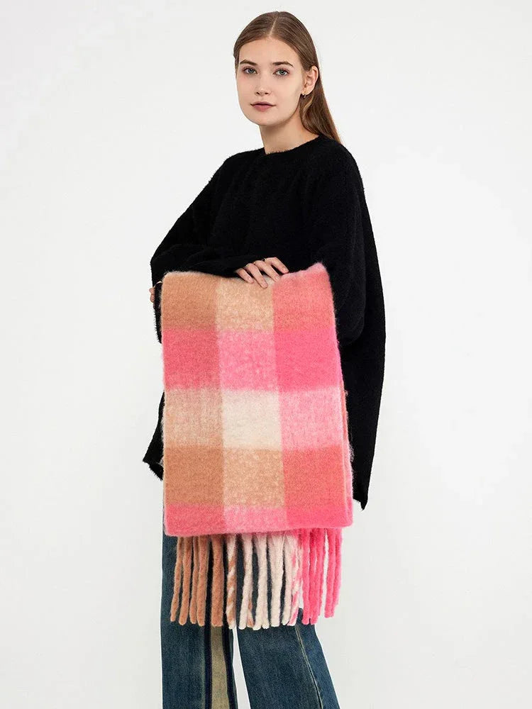 Woman holding a pink and tan plaid scarf with fringe.