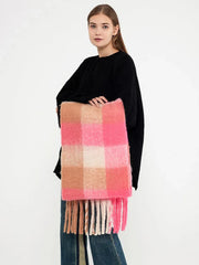 Woman holding a pink and tan plaid scarf with fringe.