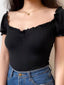 Close-up of a woman wearing a black ribbed knit top with a sweetheart neckline and ruffled trim.