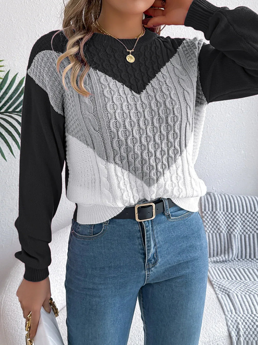 Front view of a woman in a color block chevron cable knit sweater and blue denim jeans.