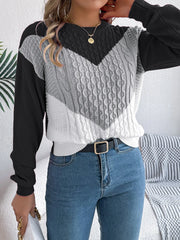 Front view of a woman in a color block chevron cable knit sweater and blue denim jeans.