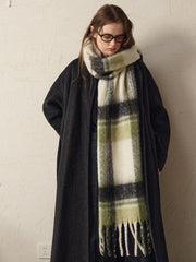 woman wearing a dark coat and a green and white plaid scarf, looking down