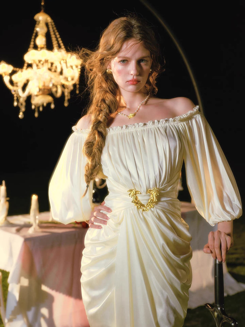 Close-up of a woman in a cream satin dress with an off-the-shoulder neckline and puffy sleeves, featuring a gold belt buckle.