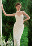 Woman in a cream satin mermaid gown with sweetheart neckline and floral embellishments, leaning against a white pillar outdoors.