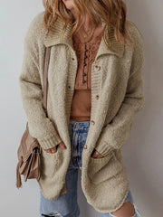 Close-up of a woman wearing a long beige knit cardigan over a brown henley top and blue jeans, with hands in pockets