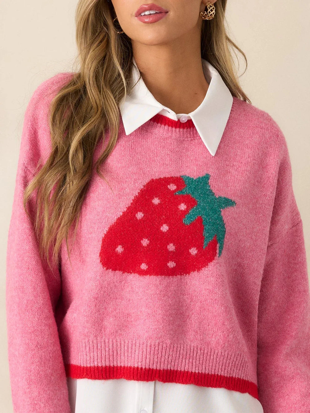 Close-up of a woman wearing a pink cropped sweater with a strawberry graphic over a white collared shirt.