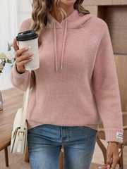 Woman wearing a pink knit hoodie and blue jeans, holding a coffee cup and a white purse.