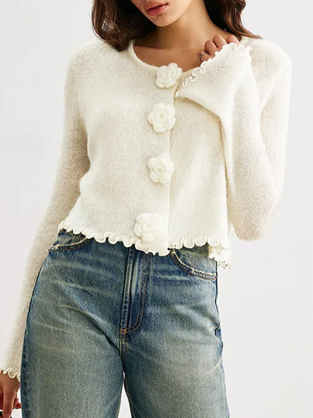 Back view of a woman wearing a white cropped knit cardigan with ruffled hem.