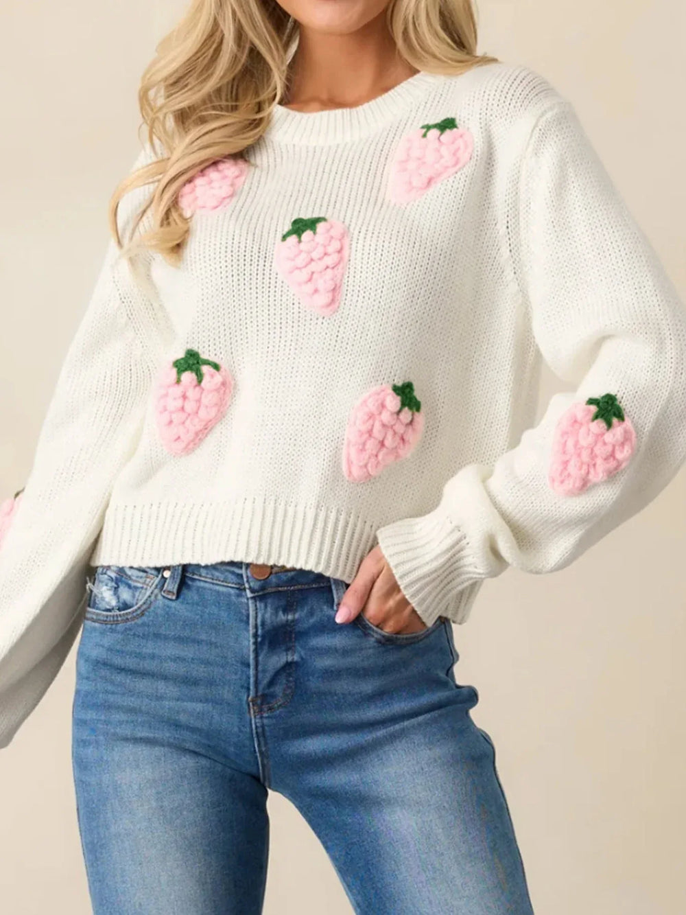 Front view of a white cropped knit sweater adorned with pink strawberry appliques, paired with blue denim jeans.