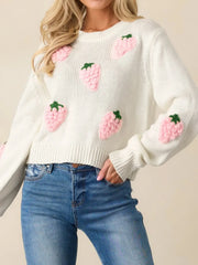 Front view of a white cropped knit sweater adorned with pink strawberry appliques, paired with blue denim jeans.