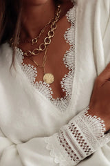 Close-up of the lace trim and gold necklaces on a white knit sweater.