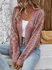 Woman sitting outdoors wearing a multicolor rainbow knit cropped cardigan, white top, and blue jeans.