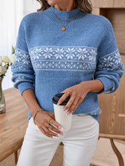 Woman wearing a blue knit sweater with a white Fair Isle snowflake and reindeer pattern, white pants, holding a coffee cup.