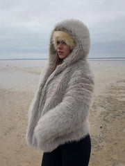 Woman standing on a beach, wearing a grey faux fur hooded coat
