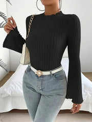 Woman in a black ribbed long-sleeve top with flared sleeves, a white belt, and light-wash denim jeans, holding a white handbag with a gold chain strap.