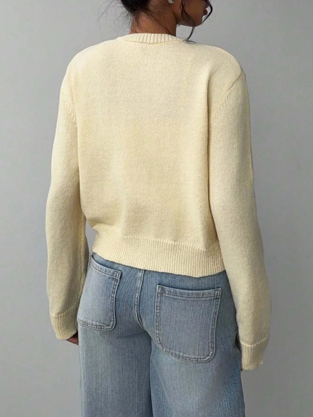 Back view of a model wearing a light yellow knit cropped cardigan and light-wash wide-leg jeans.