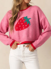Woman wearing a pink cropped sweater with a strawberry graphic and red trim, paired with white jeans.