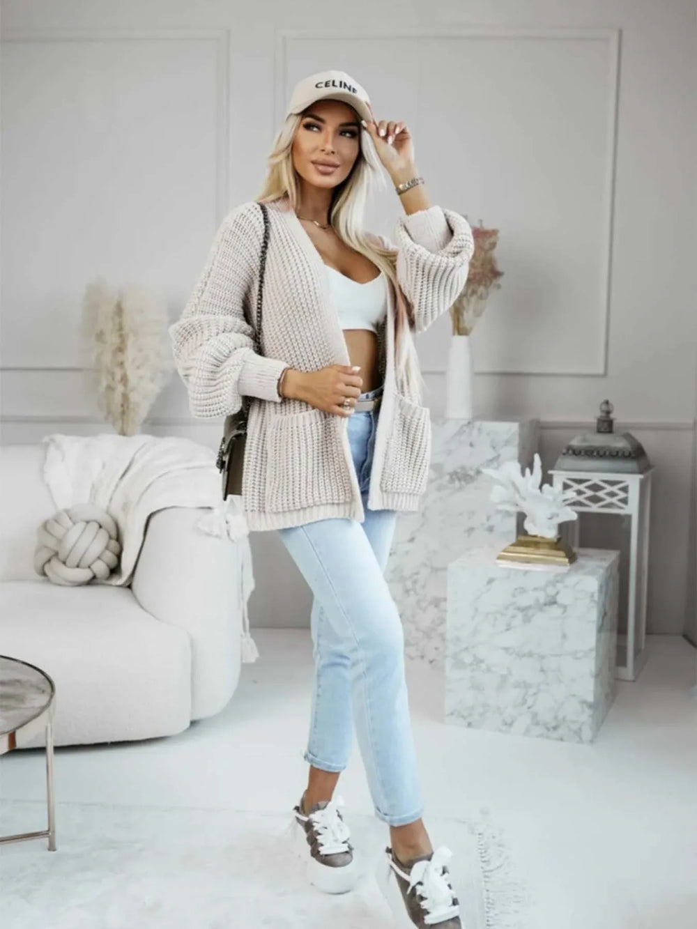 Full body shot of a woman in a beige knit cardigan, white top, and jeans