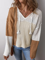 Woman wearing a color block knit sweater with a v-neck and drawstring hood, arms crossed.