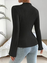 Back view of a woman wearing a black ribbed long-sleeve top with flared sleeves and light-wash denim jeans.