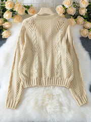 Back view of a cream-colored, open-knit, cropped cardigan with a V-neck and button-up front, laid flat on a white faux fur rug with floral accents.