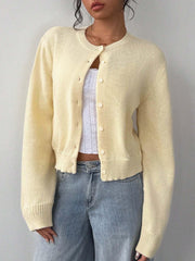 Model wearing a light yellow knit cropped cardigan with white buttons and a white lace-trimmed camisole underneath, paired with light-wash wide-leg jeans.