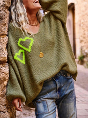 Woman leaning against a stone wall, wearing the green oversized knit sweater and distressed denim jeans, smiling.