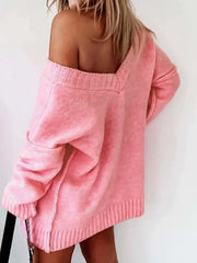 Back view of a woman wearing a pink oversized V-neck knit sweater with an off-the-shoulder design.