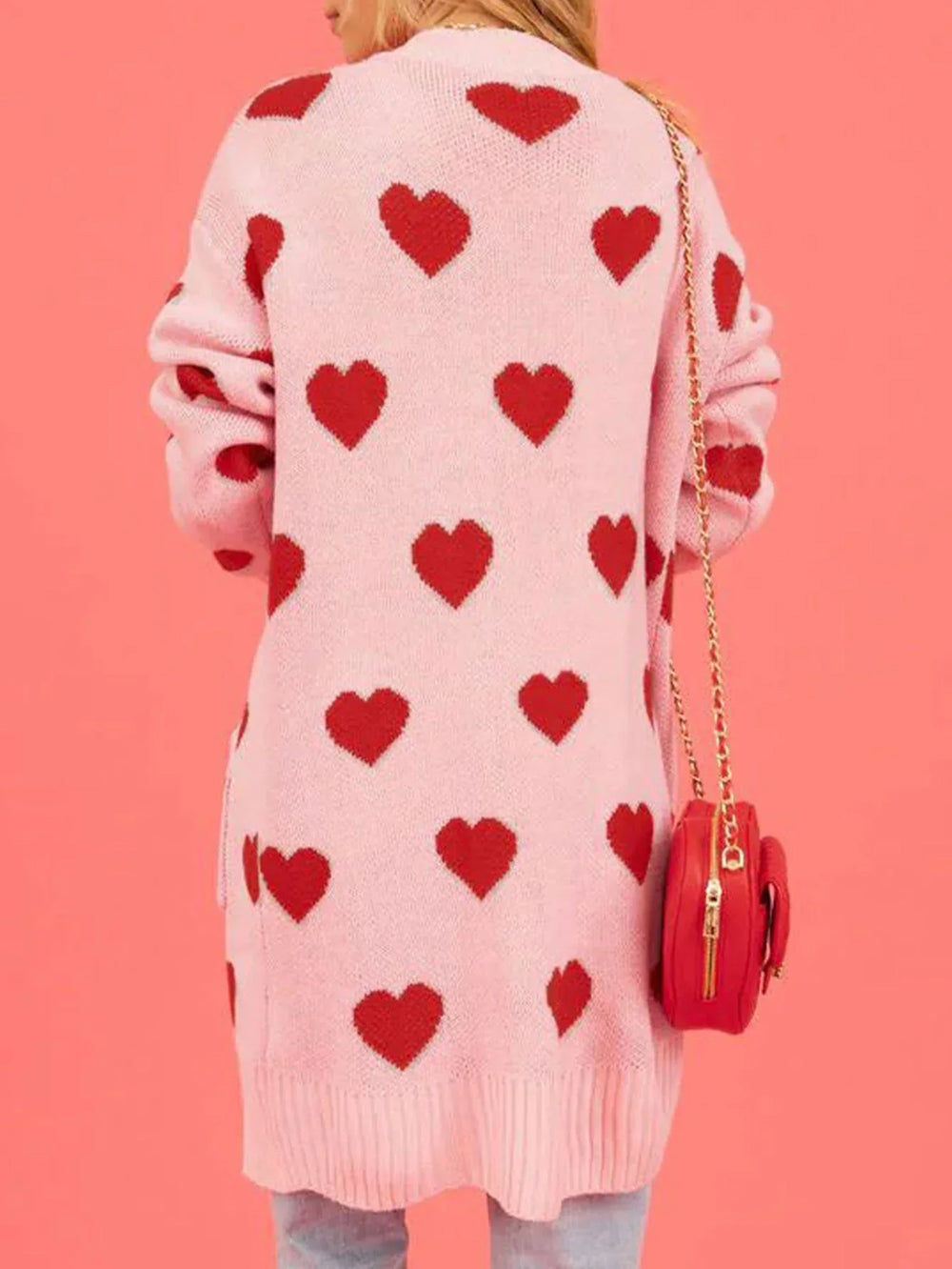 Back view of a woman wearing a pink longline cardigan with a repeating red heart pattern.