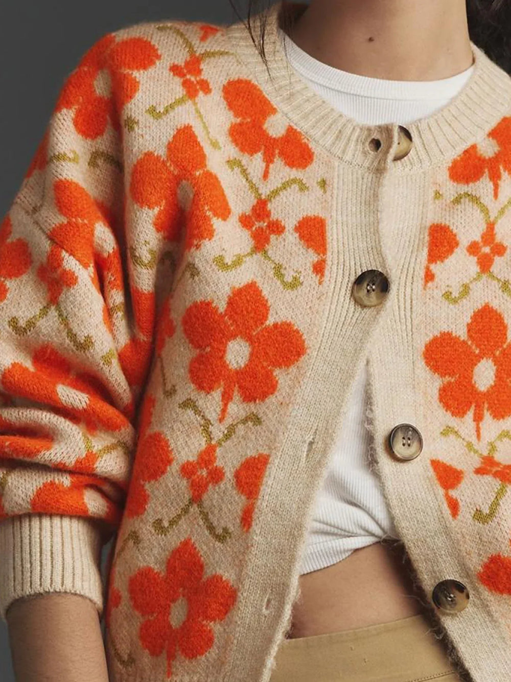 Detail of the button closure on the cream knit cardigan with an orange floral print.