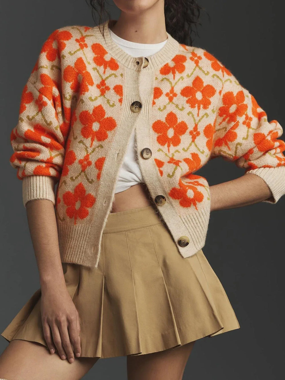 Woman wearing a cream knit cardigan with an orange floral print, paired with a tan pleated skirt.